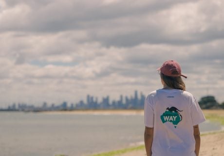Estudiante feliz con mochila frente a un paisaje australiano, promoción para estudiar inglés en Australia con visa garantizada o devolución del dinero.