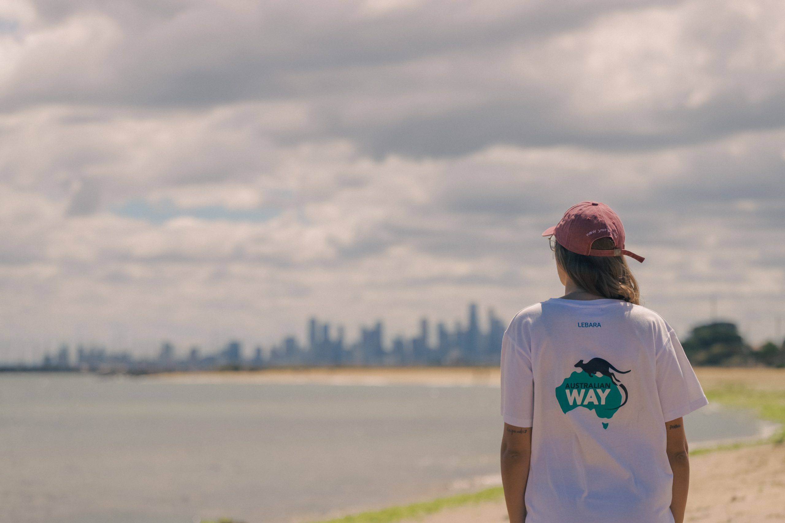 Estudiante feliz con mochila frente a un paisaje australiano, promoción para estudiar inglés en Australia con visa garantizada o devolución del dinero.
