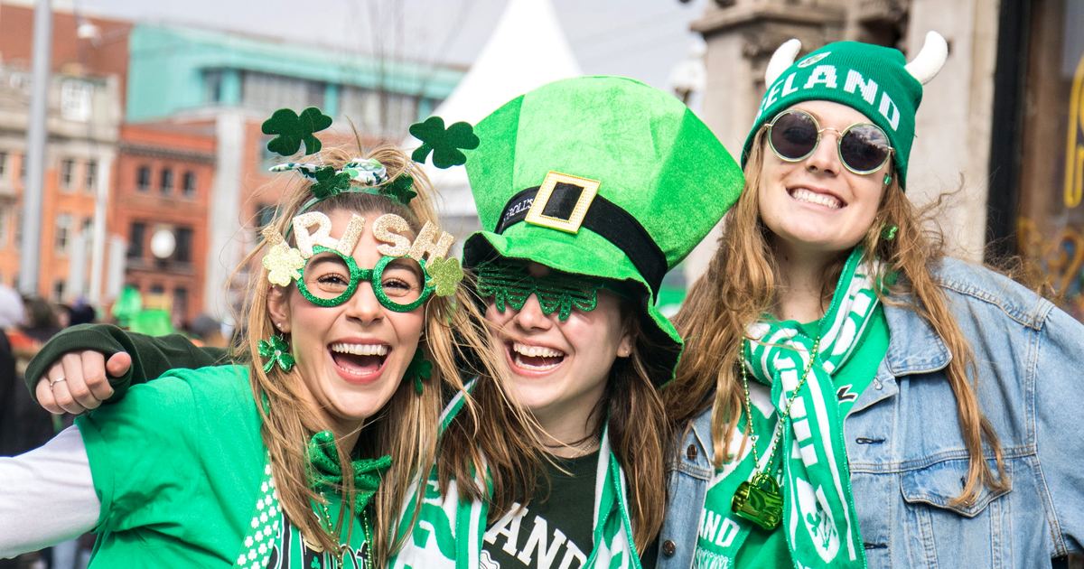 Tres jóvenes celebrando el día de San Patricio en Dublín con gorros, bufandas y gafas verdes de Irlanda